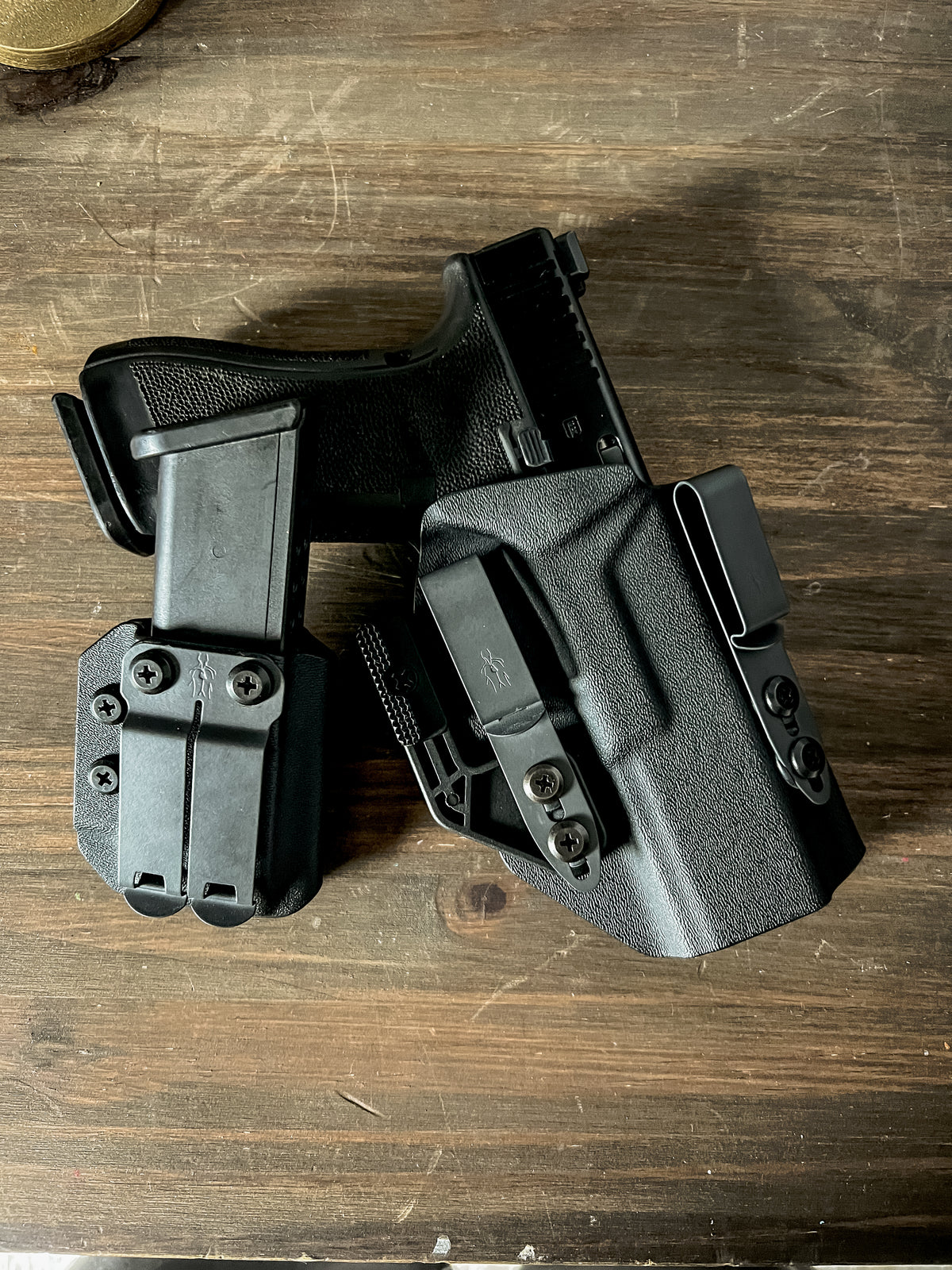 A black tactical holster containing a handgun, displayed alongside a magazine and belt clip components on a dark wooden surface.